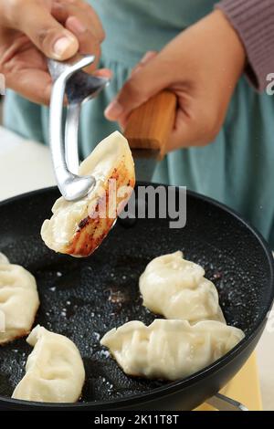 Weibliche Köchin hält Edelstahl Zangen Kochen Gyoza, japanische Knödel gefüllt mit Rindfleisch, Schweinefleisch, Chiken und gehacktem Gemüse Stockfoto