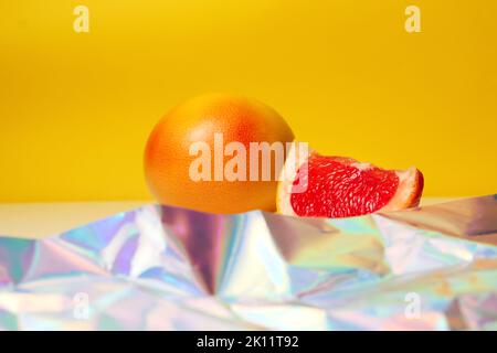 Unschärfe ganz und Stück einer roten Grapefruit auf gelbem Hintergrund und modernen Vordergrund. Gesundes Lebensmittelkonzept. Frischer Orangensaft. Vegan, vegetarisch Stockfoto