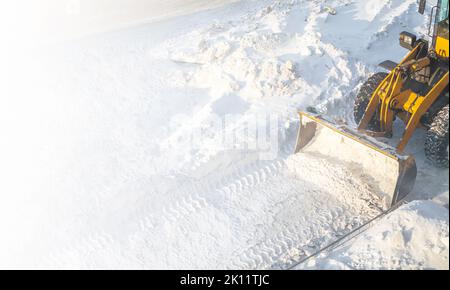 Ein großer orangefarbener Traktor entfernt Schnee von der Straße und räumt den Bürgersteig frei. Reinigung und Räumung der Straßen in der Stadt vom Schnee im Winter. Schneeräumung A Stockfoto