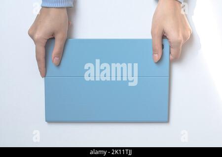 Ein Tablet in einer blauen Hülle auf einem weißen Schreibtisch. Die Hände des Mädchens halten ein Tablet. Draufsicht Stockfoto