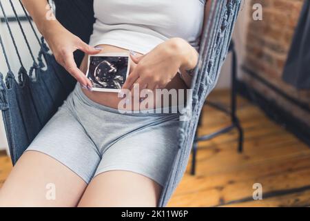 Eine kaukasische Schwangerin mit einem Ultraschallbild auf ihrem Babybauch. Hochwertige Fotos Stockfoto