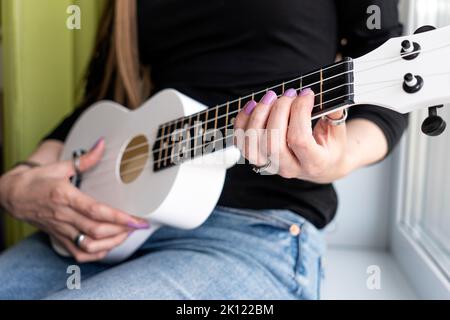 Mädchen zu Hause sitzend lernt Ukulele mit Online-Lektionen zu spielen. Stockfoto