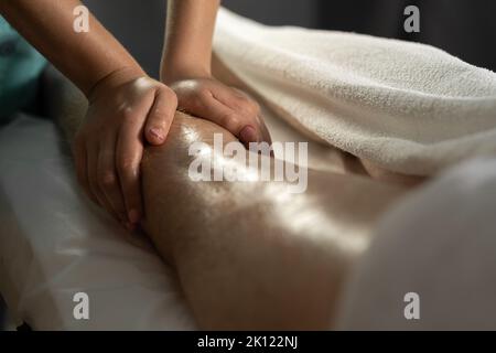 Sportmassage. Weibliche Physiotherapeutin massiert die Beine eines jungen männlichen Athleten. Nahaufnahme Masseur Hände tun Fußmassage. Stockfoto