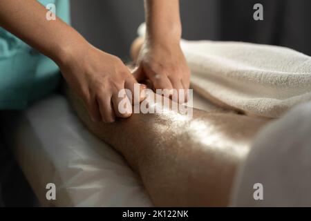 Sportmassage. Weibliche Physiotherapeutin massiert die Beine eines jungen männlichen Athleten. Nahaufnahme Masseur Hände tun Fußmassage. Stockfoto