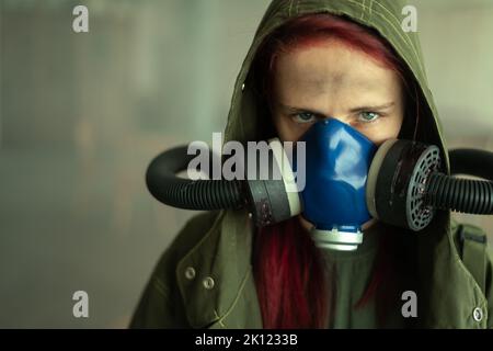 Eine junge, überlebende Frau mit einer Gasmaske, die vor ihr auf den Hintergrund blickt und ein apokalyptisches Kriegsgebiet umgibt. Traurige Frau atmet Oxy Stockfoto