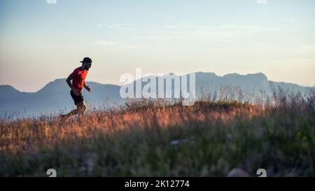 In einem hügeligen Sonnenuntergang auf bunten Wiesen läuft ein junger sportlicher Mann alleine Stockfoto