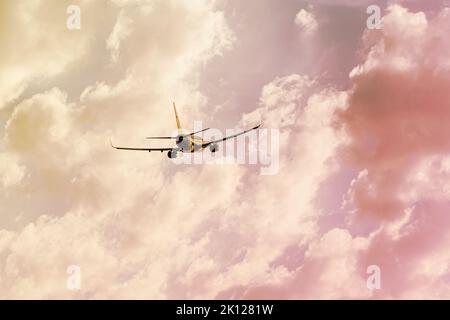 Silhouette eines Flugzeugs, das bei Sonnenuntergang hoch in den Himmel abfliegt, mit einem warmen Schatten von Wolken Stockfoto