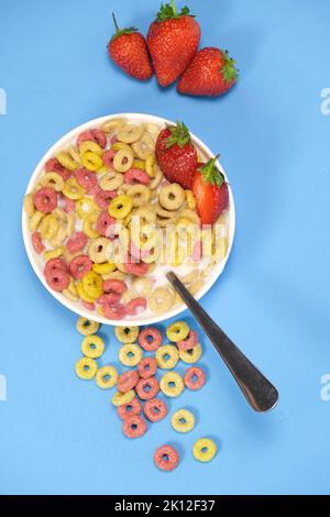 Schnelles Frühstückszerealien - Ringe mit Milch und Erdbeeren auf blauem Hintergrund. Stockfoto