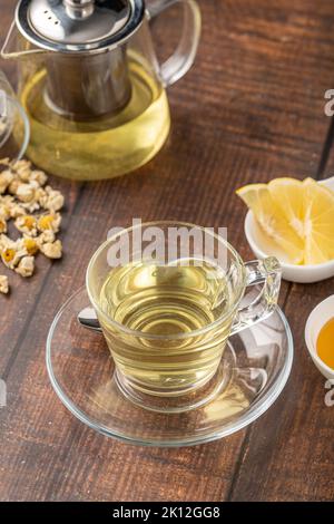 Entspannender Kamillentee in einer Glasschale mit Zitronenscheiben und Honig daneben auf einem Holztisch. Stockfoto