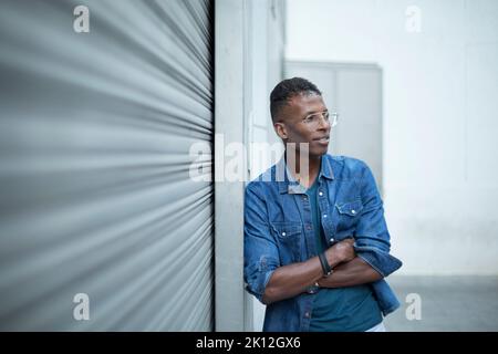 Porträt eines abgelenkten afrikanischen Mannes, der sich an einer Wand auf der Straße lehnt Stockfoto