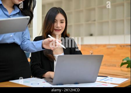 Professionelle asiatische Geschäftsfrau oder Finanzmanagerin, die ihre neuen Mitarbeiter ausbilden und die Arbeitszuweisung auf dem Laptop überprüfen. Abgeschnitten und Nahaufnahme Stockfoto