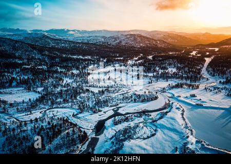 Winterlandschaft des Setesdal in Norwegen - Panoramablick bei Sonnenuntergang mit schneebedeckten Hügeln und einem gefrorenen Fluss Stockfoto