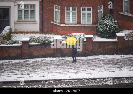 Ein Fußgänger mit gelbem Regenschirm, der im Winterschnee auf der Londoner Straße läuft Stockfoto