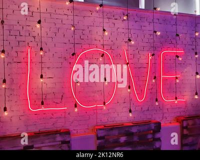 Pinkkarmesinrot mit Neonbeschriftung „Love“ und beleuchteten Retro-Glühbirnen im Dunkeln, im Restaurant oder Café. Vorderansicht, Nahaufnahme Stockfoto