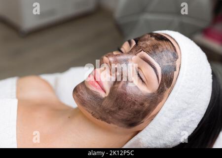 Kosmetologe, der schwarze Maske auf hübsches Frauengesicht mit schwarzen Handschuhen aufträgt, wunderschöne Frau im Spa, die Gesichtsbehandlungen hat Stockfoto