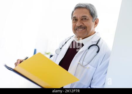 Porträt eines lächelnden männlichen Arztes aus der Birazialebene, der die Patientenakte hält Stockfoto