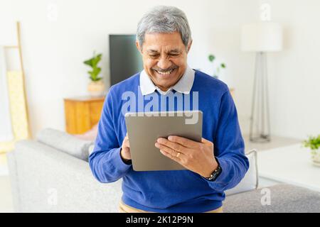 Lächelnder älterer Birazialmann, der im Wohnzimmer zu Hause ein Tablet benutzt Stockfoto