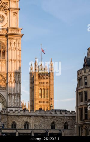 Im Zentrum von London fliegt der Union Jack halbmast über den Victoria Tower, Teil des Palace of Westminster, um den jüngsten Tod von Königin Elizabeth II. Zu markieren Ein Teil der Westminster Abbey ist im Vordergrund zu sehen Stockfoto