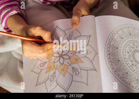 Frau Färbung Antistress Seite. Weibliche Hand Malerei Mandala. Weibliche Malerei Mandalas, um Stress zu bekämpfen. Entspannendes Hobby mentales Wohlbefinden und Kunsttherapie. Frau malt Skizze, meditative Prozess der Malvorlagen. Selbstausdruck durch Kunst Stockfoto