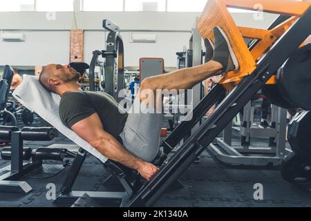 Muskulöser Mann, der an der Beinpresse arbeitet, voller Schuss. Hochwertige Fotos Stockfoto