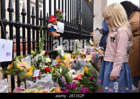 Ein Kind sieht sich die Blumenverehrungen an, die für Ihre Majestät Königin Elizabeth II. Im Buckingham Palace in London hinterlassen wurden. Stockfoto