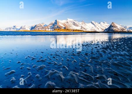 Wellen des kalten Meeres krachen am Strand mit schneebedeckten Bergen im Hintergrund, Fredvang, Nordland, Lofoten Islands, Norwegen, Europa Stockfoto