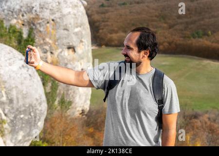 Junge Erwachsene glücklich kaukasischen bärtigen Mann genießen Lächeln und machen Selfie Foto Trekking im Freien Hügel und Berg. Männliche Touristen wandern draußen Stockfoto