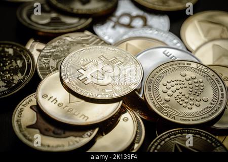 Nahaufnahme eines goldenen Bitcoins in einem Stapel, unter anderem verschiedener digitaler Kryptowährungen. Stockfoto
