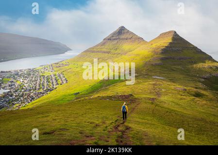 Wanderer mit gelber Jacke geht den Berg Klakker hinunter, Klaksvik, Borooy Island, Färöer Islands, Dänemark, Europa Stockfoto