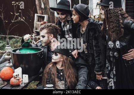 Beängstigende Familie, Mutter, Vater, Töchter, die Halloween feiern. Kessel des Trank. Erschreckende schwarze Schädel Halbgesicht Make-up, Hexe Kostüme, stilvolle Bild Stockfoto