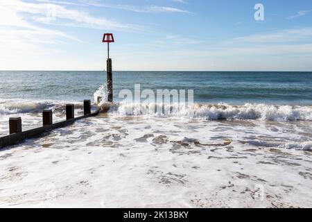 Im Sommer brechen die Wellen am Strand von Bournemouth, Dorset, England, auf und plätschern über einen groynen Marker Stockfoto