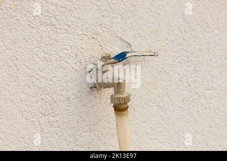 Wasserhahn an der Wand. Rostiger blauer Gartenhahn mit angeschlossenem Schlauch. Stockfoto