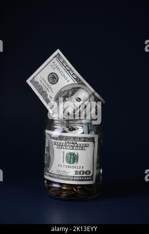 Dollar in einem Glasgefäß mit Münzen auf dunkelblauem Hintergrund. Sparkonzept Stockfoto