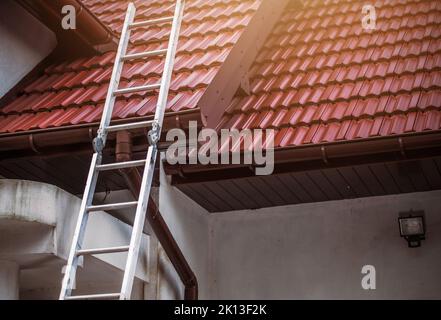 Konstruktion Verlängerung Leiter schief gegen den Rand des Daches mit roten Keramikfliesen bedeckt. Altes Wohnhaus Reparatur- und Renovierungsarbeiten in Pro Stockfoto