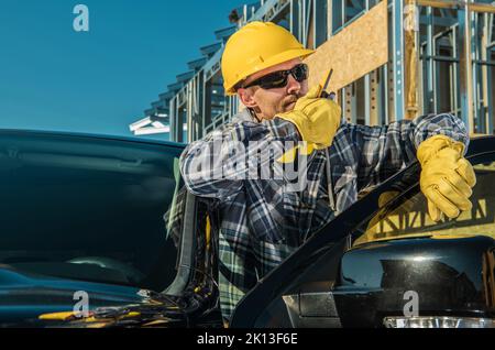 Kaukasischer Mann mittleren Alters, der neben seinem Pickup Truck steht und mit anderen Arbeitern über den Citizens' Band Radio Sender kommuniziert. Bauvorhaben Stockfoto
