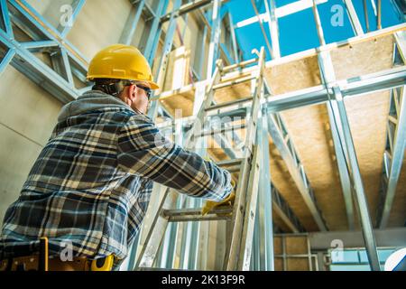 Foto von einem professionellen Bauarbeiter mit gelbem Sicherheitshelm, der die Verlängerungsleiter besteigte, um den nächsten Stock bei New Commer zu erreichen Stockfoto