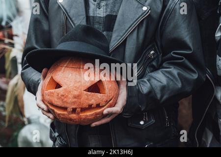 Oranger Kürbis für halloween in schwarzem Hut, Jack-o-Laterne mit gruselig geschnitzten Augen, Mund. Heu, Heuhaufen in der Nähe der Scheune. DIY Haus, Straßendekoration, enterta Stockfoto