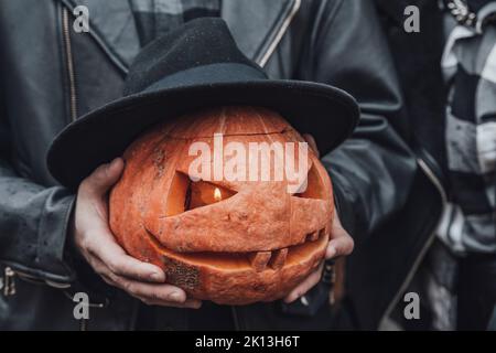 Oranger Kürbis für halloween in schwarzem Hut, Jack-o-Laterne mit gruselig geschnitzten Augen, Mund. Heu, Heuhaufen in der Nähe der Scheune. DIY Haus, Straßendekoration, enterta Stockfoto