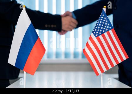 Nahaufnahme von zwei Geschäftsleuten, die sich vor uns die Hände schüttelten. Russische Flaggen auf dem Tisch Stockfoto