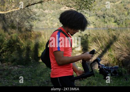 Mann mit Afro, der einen Gimbal mit Kamera auf dem Land hält Stockfoto