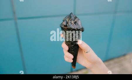 Schwarzes kohlegrundes Eis in weiblicher Hand auf blauem Hintergrund. Stockfoto