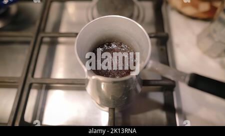 Türkischer Kaffee kocht über von CEZVE. Dichter Schaum in der Kaffeemaschine auf einem Gasherd. Stockfoto