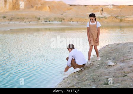 Kinder waschen sich im See die Hände, Bruder und Schwester ruhen sich in der Natur aus. Stockfoto