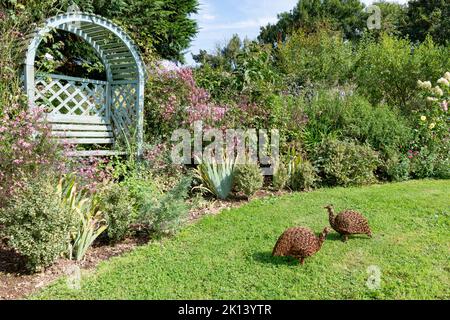 Hübscher bogenförmiger Gartensitz in einem englischen Landgarten mit zwei Vogelskulpturen Stockfoto