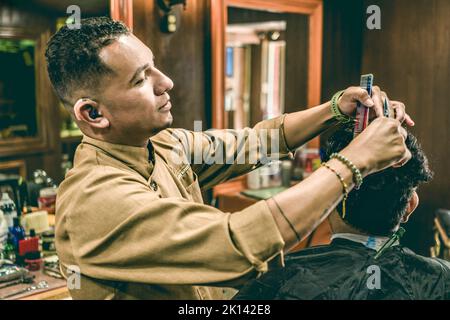 Junger behinderter Barbier mit Hörgerät, der in einem Friseurladen Haare eines Mannes schneidet. Stockfoto