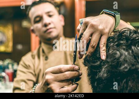 Der junge Barbier, der scharfe professionelle Scheren hält, schneidet in einem Friseurladen die Haare aus dem Blickfeld. Stockfoto