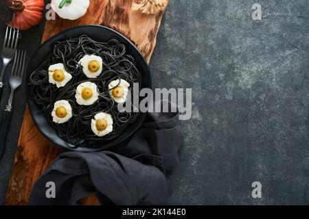 Halloween Party italienische schwarze Pasta dekoriert Horror Oliven wie Augen auf schwarzem Teller auf alten dunklen Tisch Hintergrund. Monster Gesicht von Pasta. Halloween Stockfoto