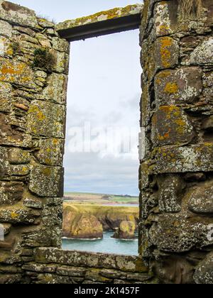 Blick durch das Fenster einer alten Burgruine über die zerklüftete schottische Küste, Stockfoto