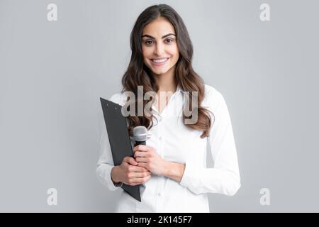 Lächelnde junge Frau als Reporterin mit Mikrofon und Klemmbrett. Journalistin mit Mikrofon und Clipboard. Stockfoto