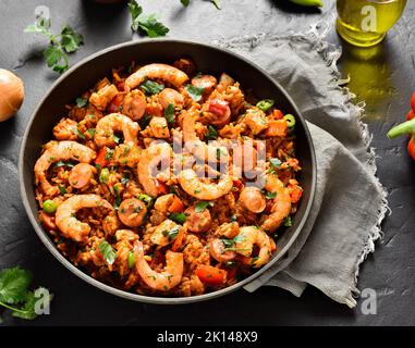 Kreolischer Jambalaya mit Huhn, geräucherten Würstchen und Gemüse in einer Pfanne auf schwarzem Stein. Nahaufnahme Stockfoto